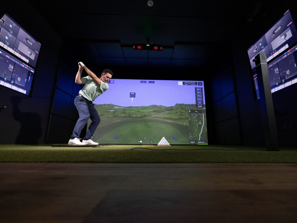 Person playing golf in a simulator with screens on either side